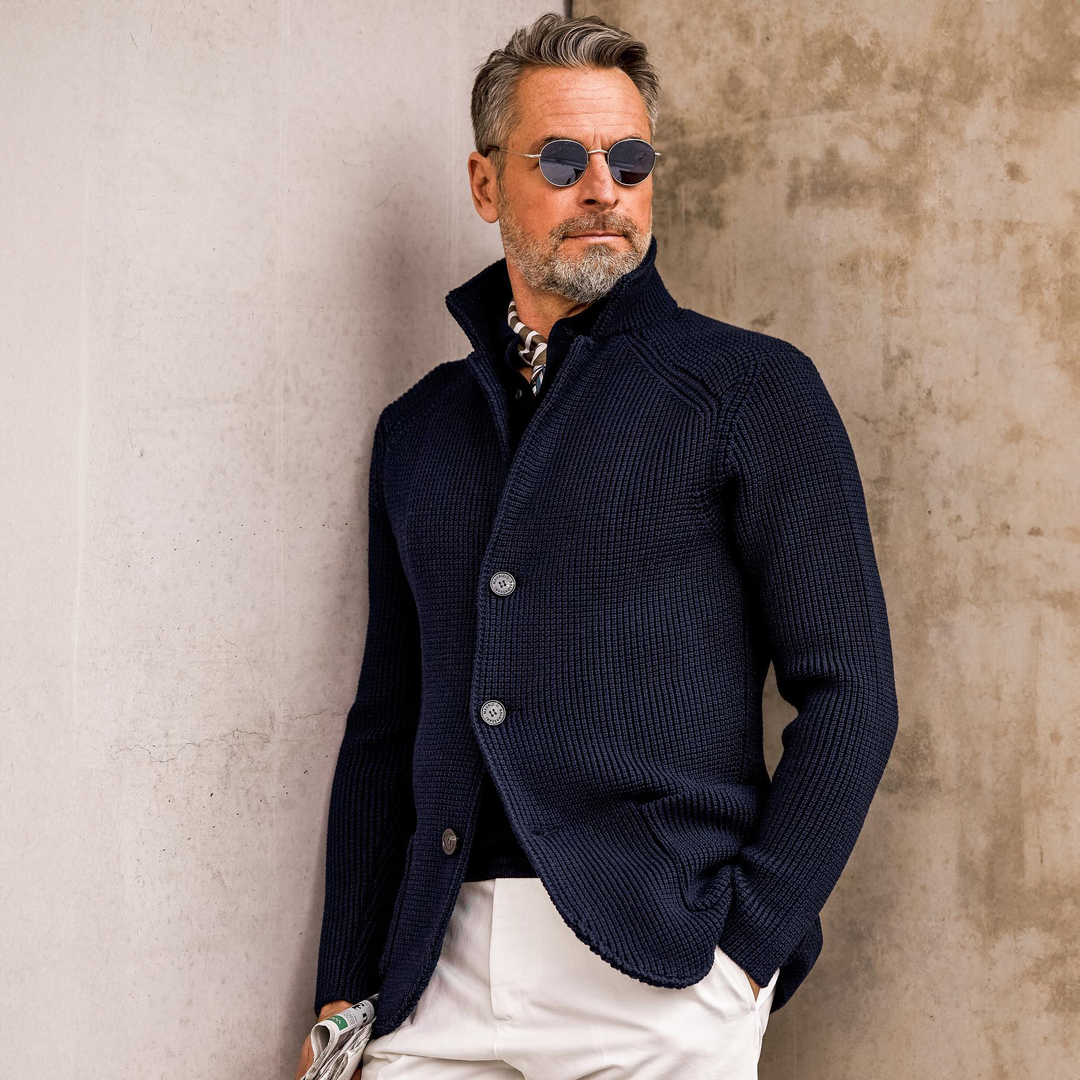 Man wearing navy knit cardigan leaning against wall with sunglasses, lifestyle shot